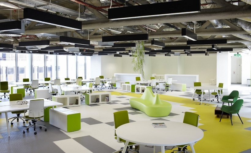 A large office space with white tables and green chairs Description automatically generated